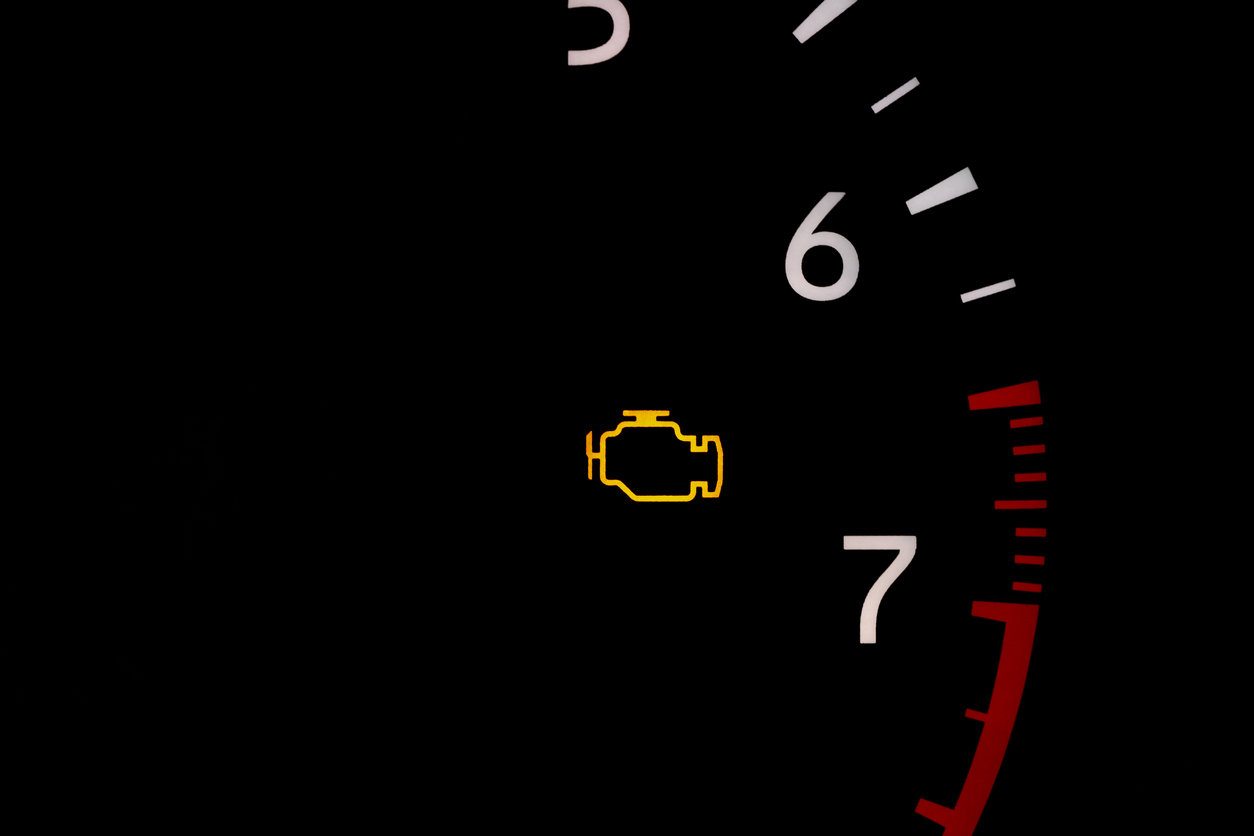 Check engine light illuminated in yellow is shown close up on a tachometer with white numerals