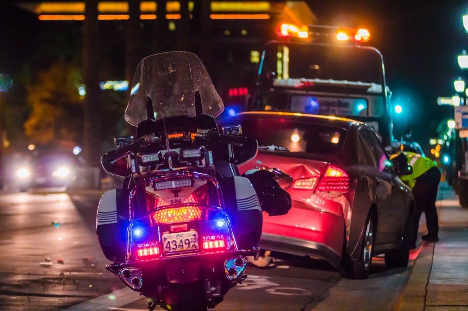 Police motorcycle parked behind a crashed car on a city street at night.