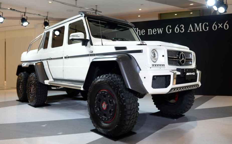 A white Mercedes-Benz G63 6x6 pickup is shown parked at a right front angle on a showroom floor