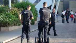 A security guard rides a Segway on a paver stone road with his back turned to the camera