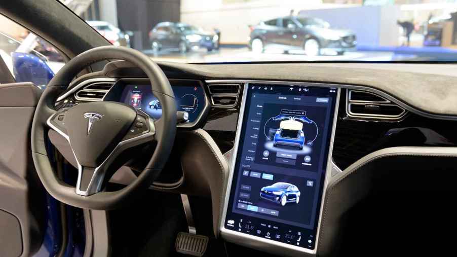 The front interior of a Tesla Model S is shown with the touch screen activated, volume control inspired by the movie This is Spinal Tap.