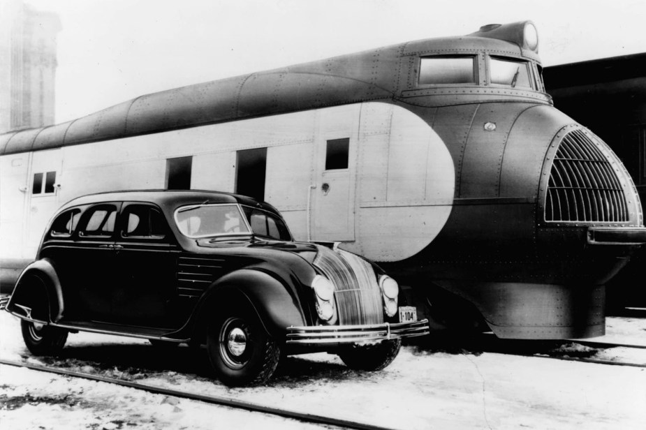 Promo photo of a 1934 Chrysler Airflow parked next to a train.