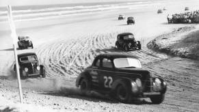 Two door coupe stock cars round the hairpin turn at Daytona Beach during inaugural NASCAR race.