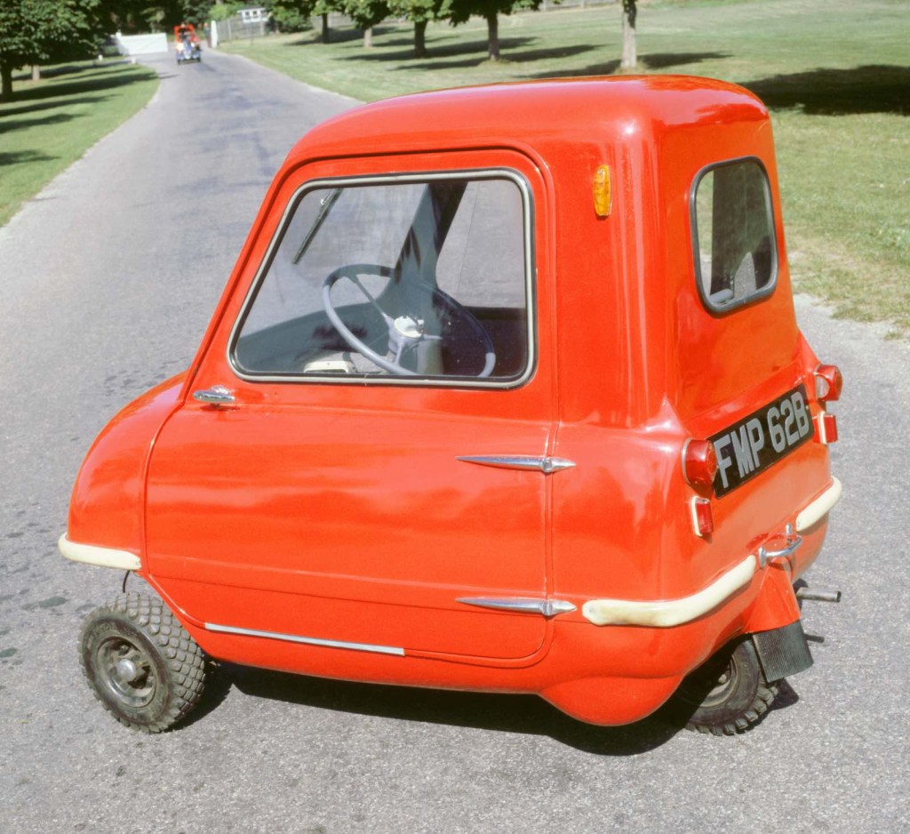 Side view of a red microcar parked on a country road.