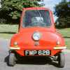 red one-seat micro car parked in front of a grass lawn