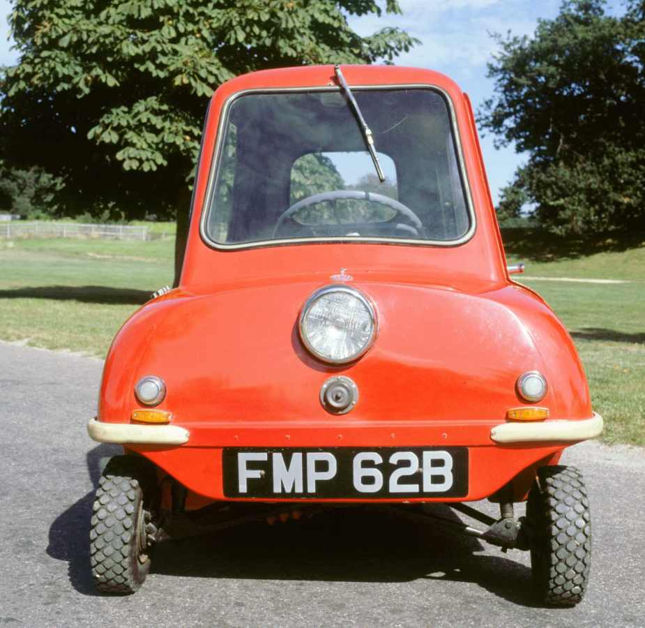 red one-seat micro car parked in front of a grass lawn