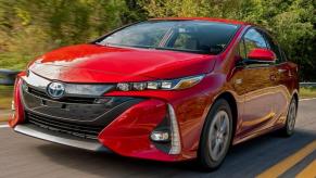 Red 2021 Toyota Prius Prime driving on a road. This is one of the most popular used PHEVs.