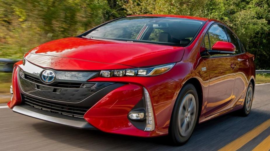 Red 2021 Toyota Prius Prime driving on a road. This is one of the most popular used PHEVs.