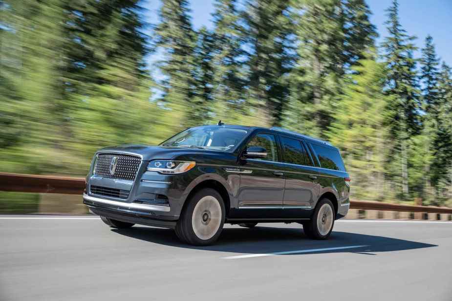 A blue 2022 Lincoln Navigator SUV driving on the read with evergreen trees in the background