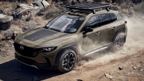 A green 2023 Mazda CX-50 with roof rack drives down a dusty trail with