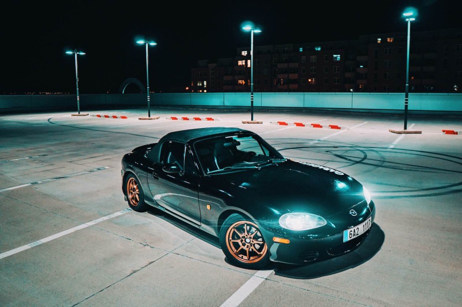 Black Mazda Miata sports car parked on the top deck of a parking garage.