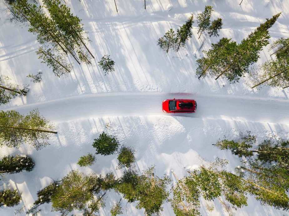 A red car drives through the snow in the woods.