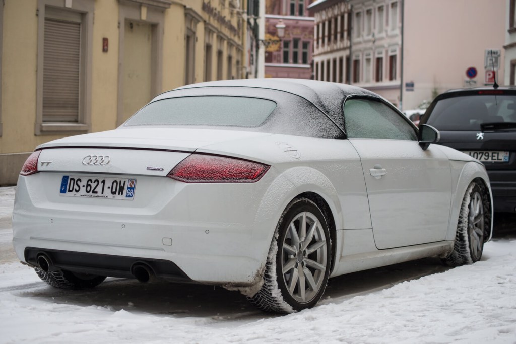 A white Audi TT rear-wheel drive sports car drives in the snow. 