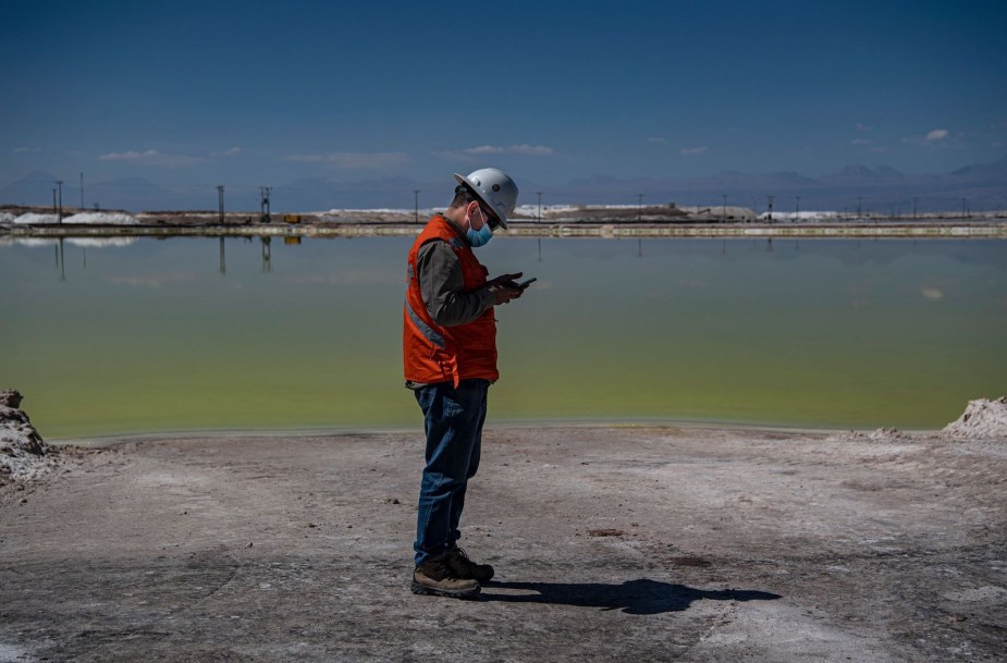 Worker at the Sociedad Quimica Minera lithium mine in Chile stands in front of a brine pool.