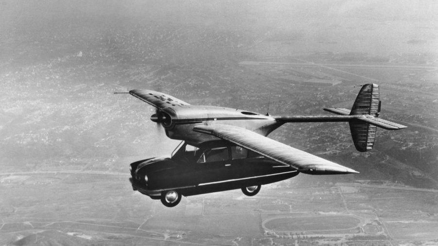 Black and white photo of a flying car with plane wings.