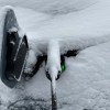 An EV charge port with charger plugged in during a snow storm covered in snow