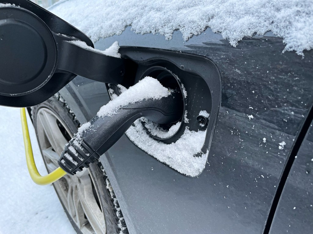 An EV charge port in close-view with charge nozzle plugged in during winter