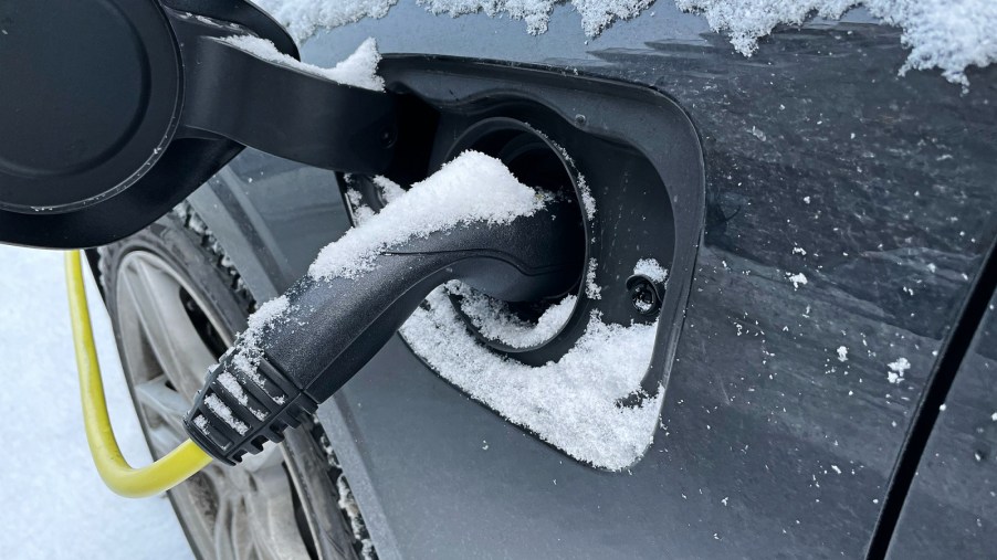 An EV charge port in close-view with charge nozzle plugged in during winter