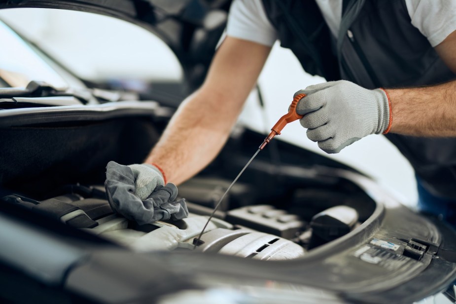 Auto mechanic uses the engine dipstick to check the level of the motor oil.