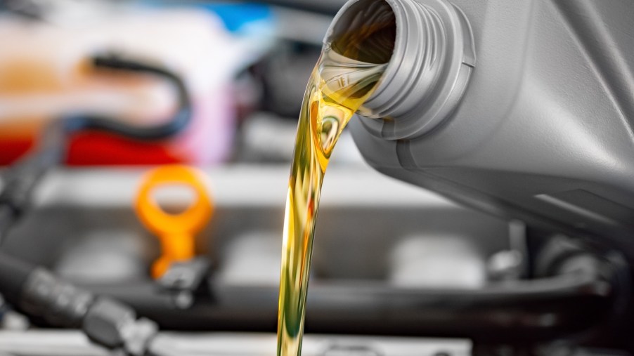 Motor oil pouring out of a jug and into a car's engine.