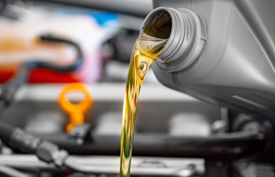 Motor oil pouring out of a jug and into a car's engine.