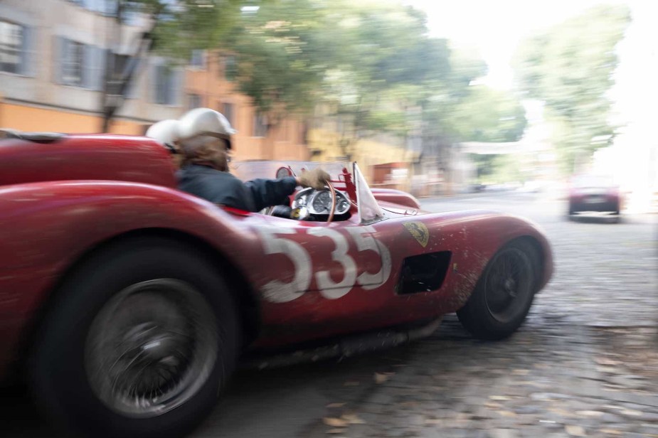 Vintage red Ferrari race car on a cobblestone street during a movie.