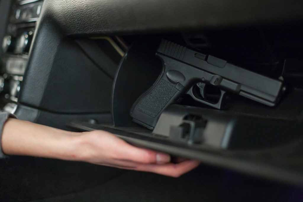 A driver reaches for a gun outside of a car safe in their glove compartment. 