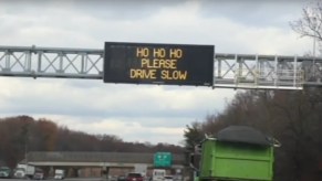 Road sign above New Jersey highway that reads "Ho Ho Ho Please Drive Slow"