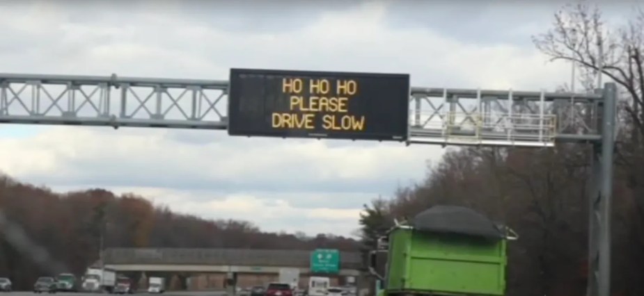 Road sign above New Jersey highway that reads "Ho Ho Ho Please Drive Slow"
