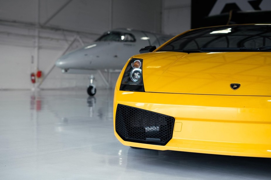 Closeup of the Lamborghini badge on the hood of a yellow Gallardo sports car, a plane visible in the background.