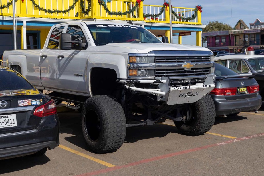 White Chevrolet Silverado 1500 pickup truck with a lift kit in a parking lot.