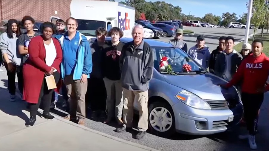 A high school shop classes poses by a car they fixed up to give to a single mom.