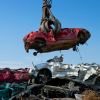 Red sedan picked up by a crane in a salvage yard