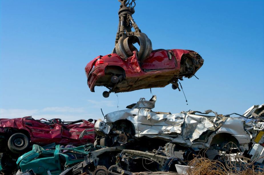 Red sedan picked up by a crane in a salvage yard