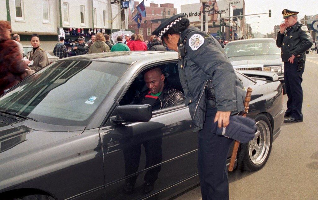 Basketball star Michael Jordan sits in his BMW 850i and signs an autograph for a police officer during Wrigley's field opening day 1993.