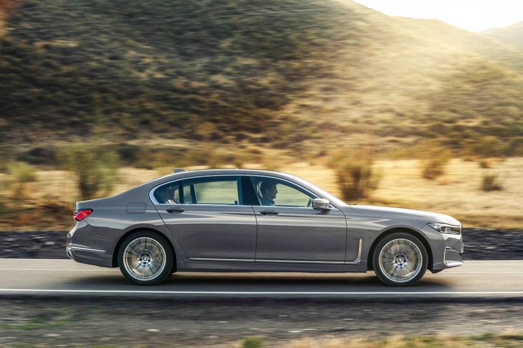 A silver BMW 7 Series luxury car drives on a mountain road.