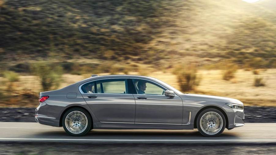 A silver BMW 7 Series luxury car drives on a mountain road.