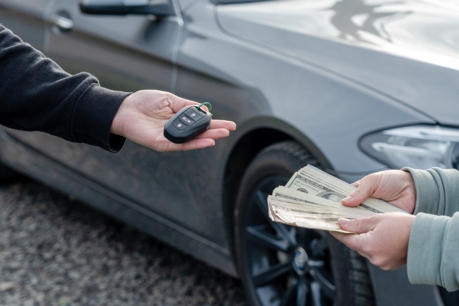 A person offers a stack of paper bills in exchange for car keys.
