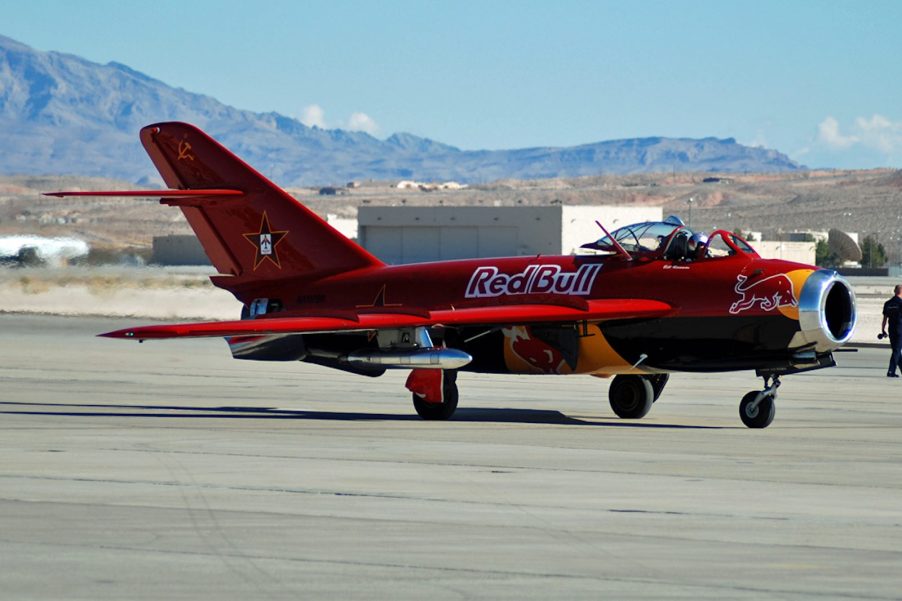 A red MIG fighter jet on a runway with the Red Bull logo on the side.