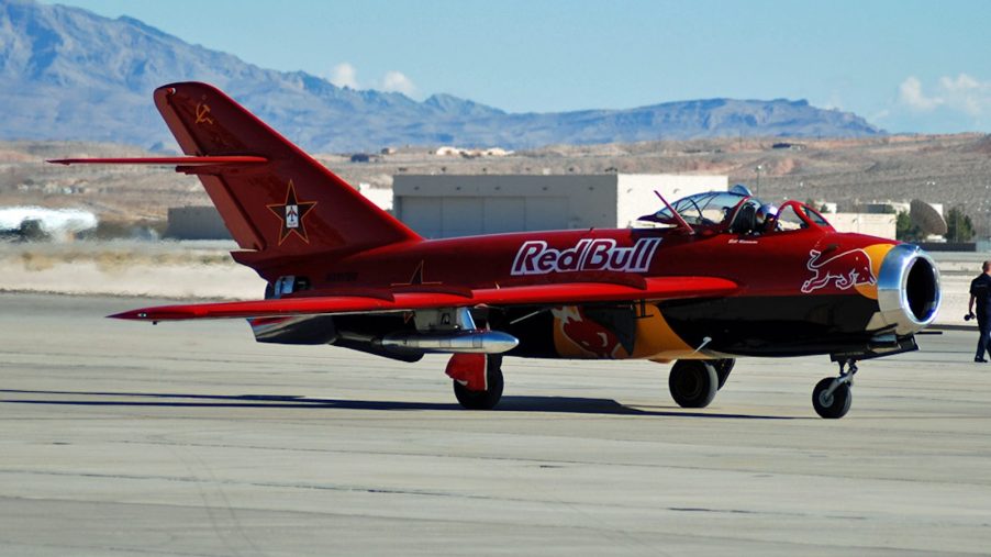 A red MIG fighter jet on a runway with the Red Bull logo on the side.