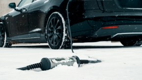 Bricked Tesla parked in the snow with its charger on the ground.