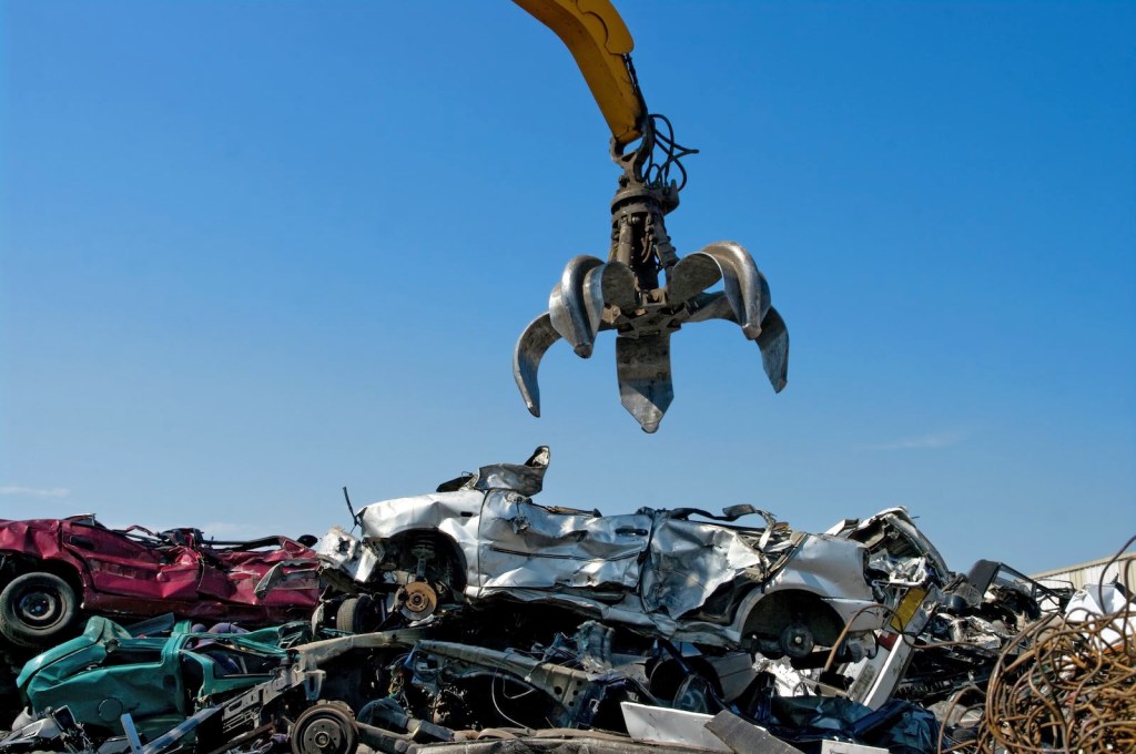 Salvage yard crane dropping a used crossover SUV onto a junk pile.