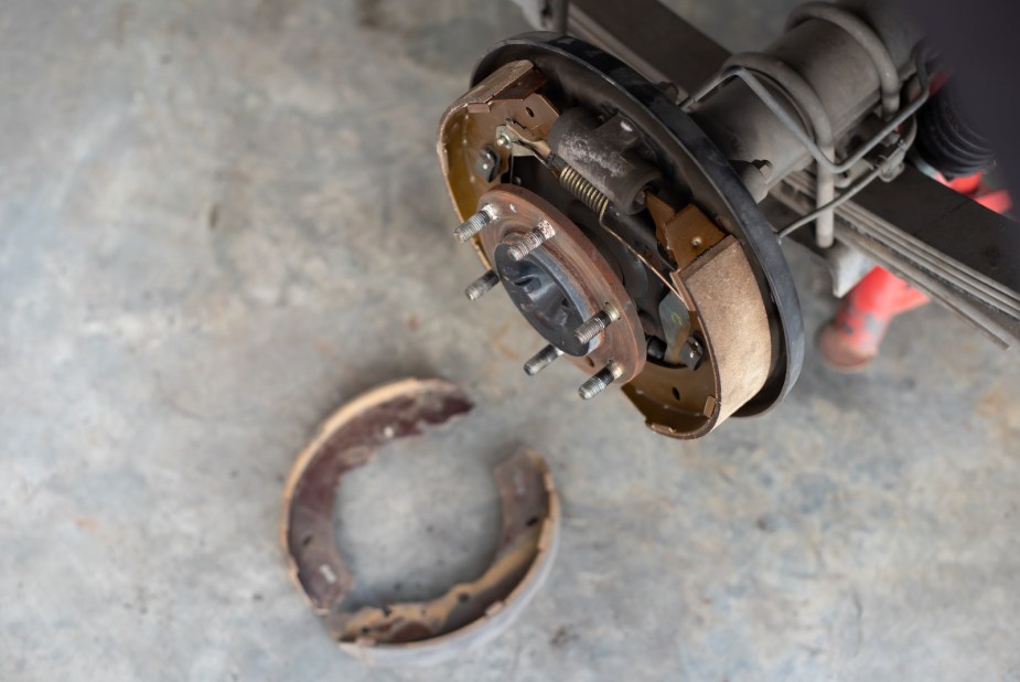 Rusty drum brake shoes and replacements sitting beneath an internal combustion car.