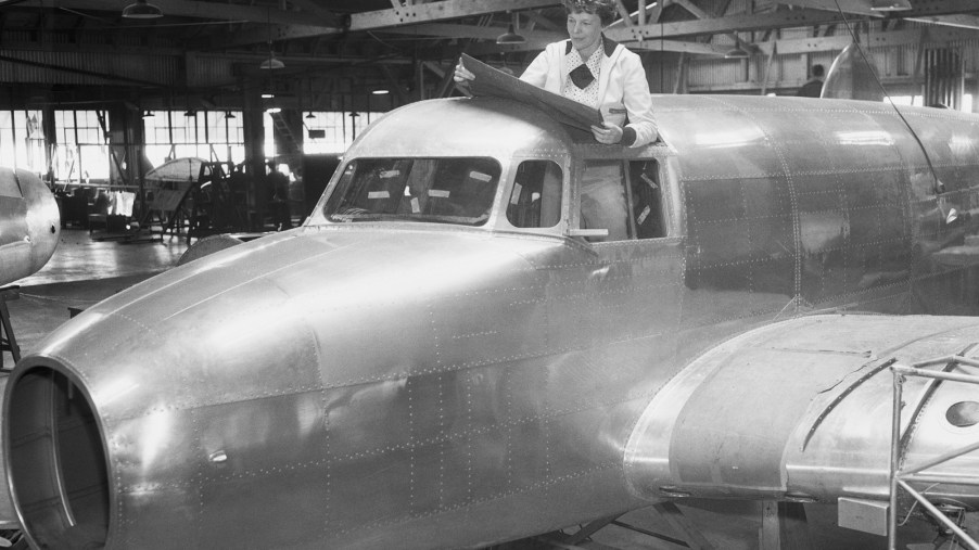 Amelia Earnhart examines blueprints while standing in the cockpit of her unfinished Lockheed Electra 10E airplane