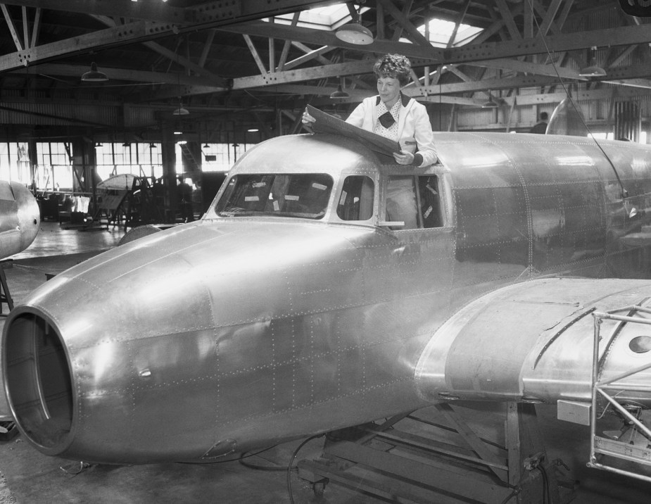 Amelia Earnhart examines blueprints while standing in the cockpit of her unfinished Lockheed Electra 10E airplane