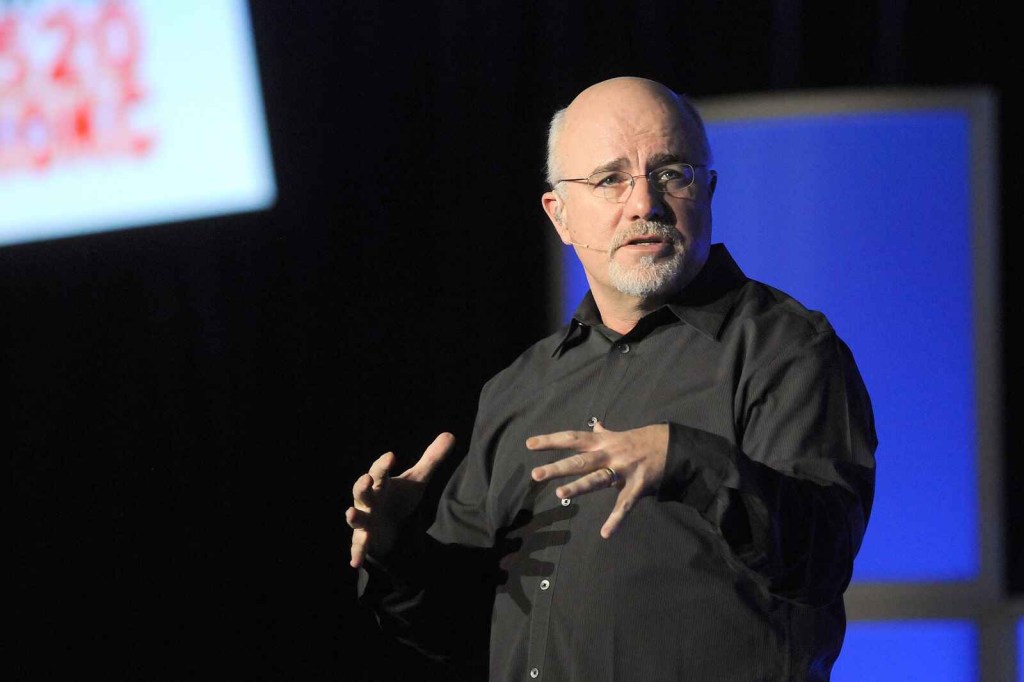 Dave Ramsey wearing glasses and a black button shirt presenting on stage in 2011