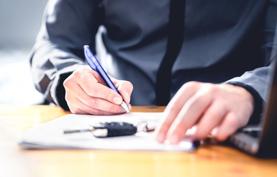 Man finishes a car financing contract on a desk, the keys nearby.