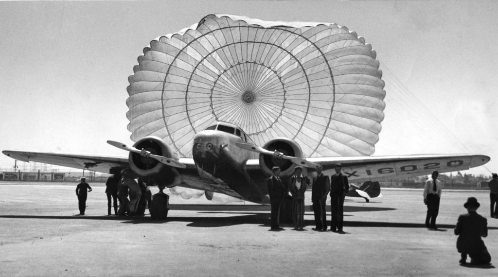 Amelia Earhart's Lockheed Electra 10E airplane with rear parachute deployed and crew standing in front