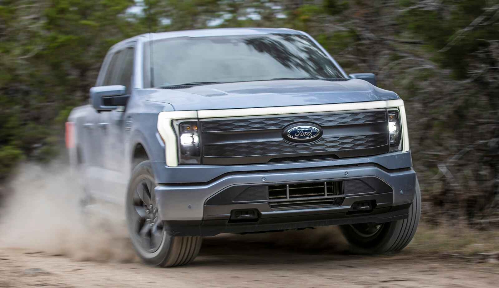 A grey Ford F-150 Lightning EV pickup truck is shown in right front close angle driving on a dusty road