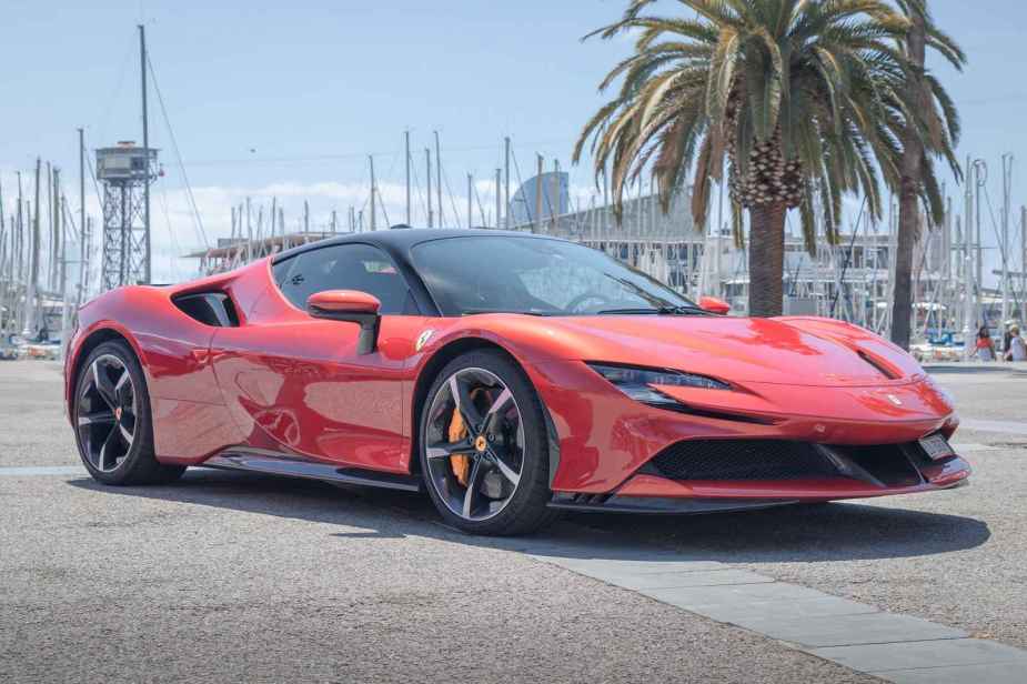 A red Ferrari SF90 Spider parked in front of a palm tree at a harbor on a sunny day